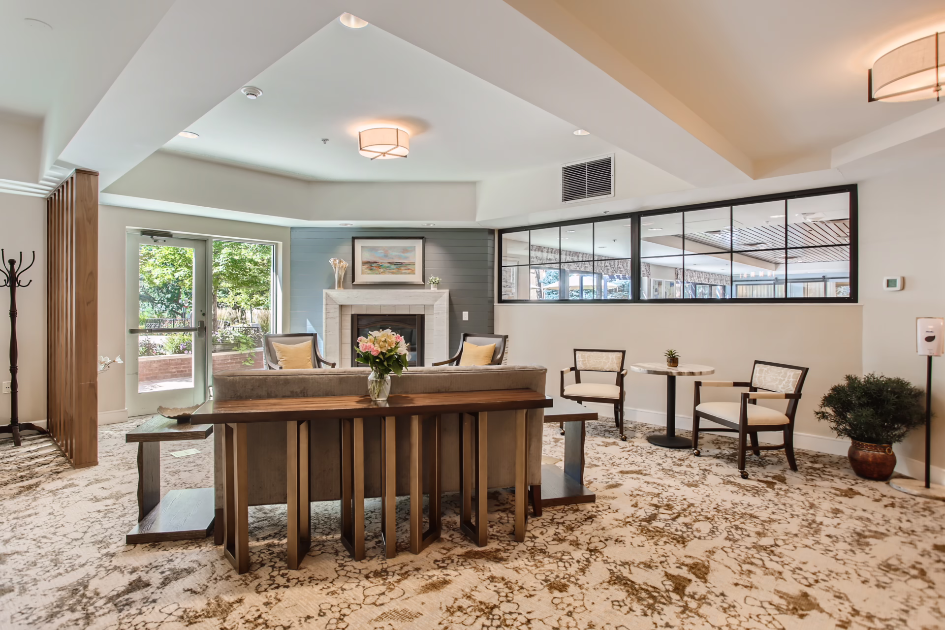 Senior living community lobby with a mirrored wall extending natural light from an adjoining outdoor patio, by Aneka Interiors